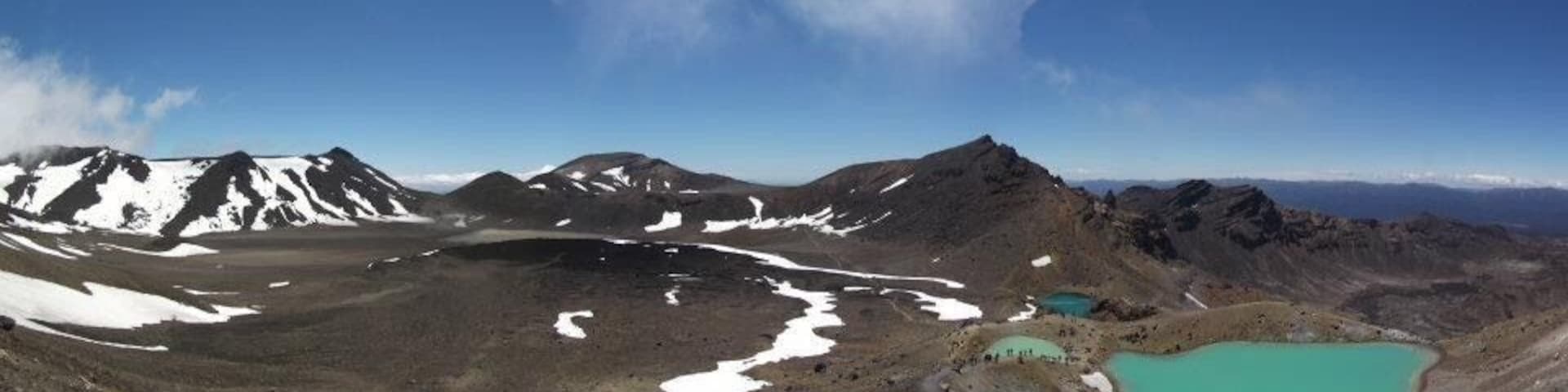 A mountainous landscape with snow patches, a turquoise lake, and a clear sky.
