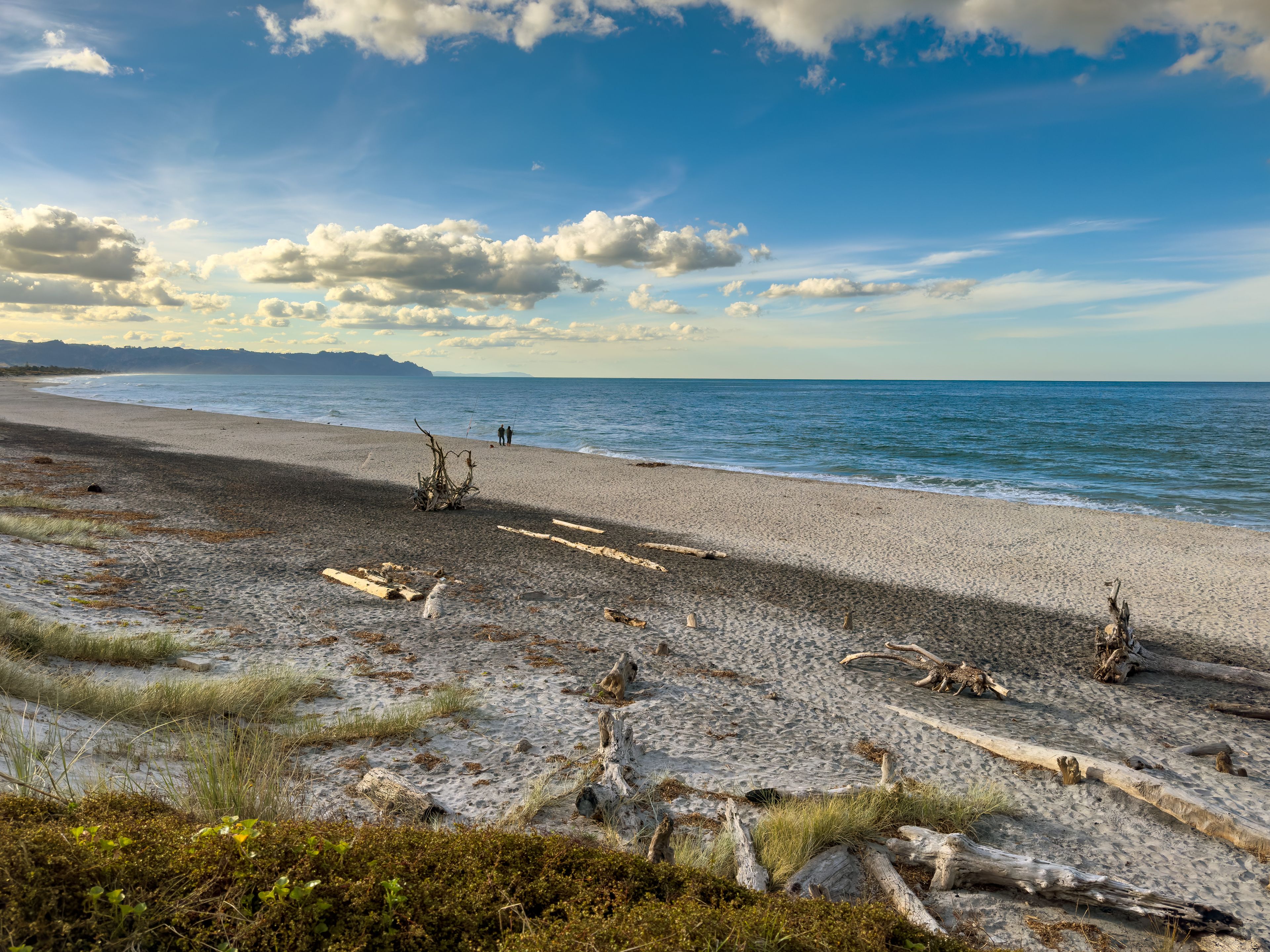 Waihī Beach, New Zealand in golden light, viewed from the south end at Bowentown. Deserted apart from two people fishing.