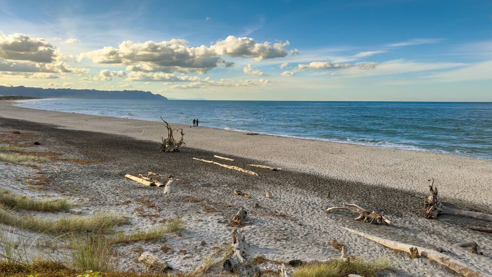 Waihī Beach, New Zealand in golden light, viewed from the south end at Bowentown. Deserted apart from two people fishing.