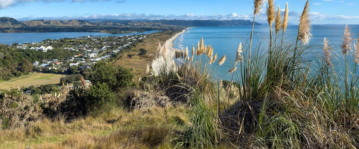 Un paysage côtier avec une plage, des maisons et des montagnes à l’horizon.