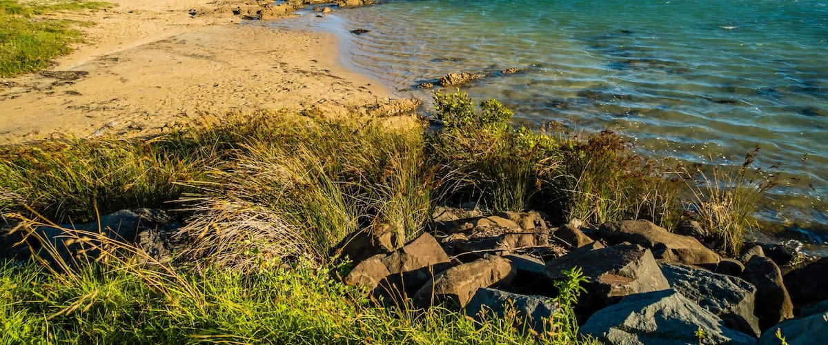 A coastal landscape with clear waters, sandy beach, and rocky outcrops.