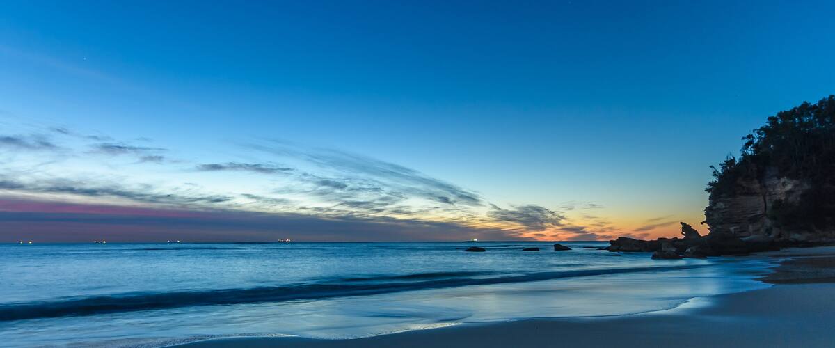 A beach with calm waves, a clear sky, and rocky cliffs.