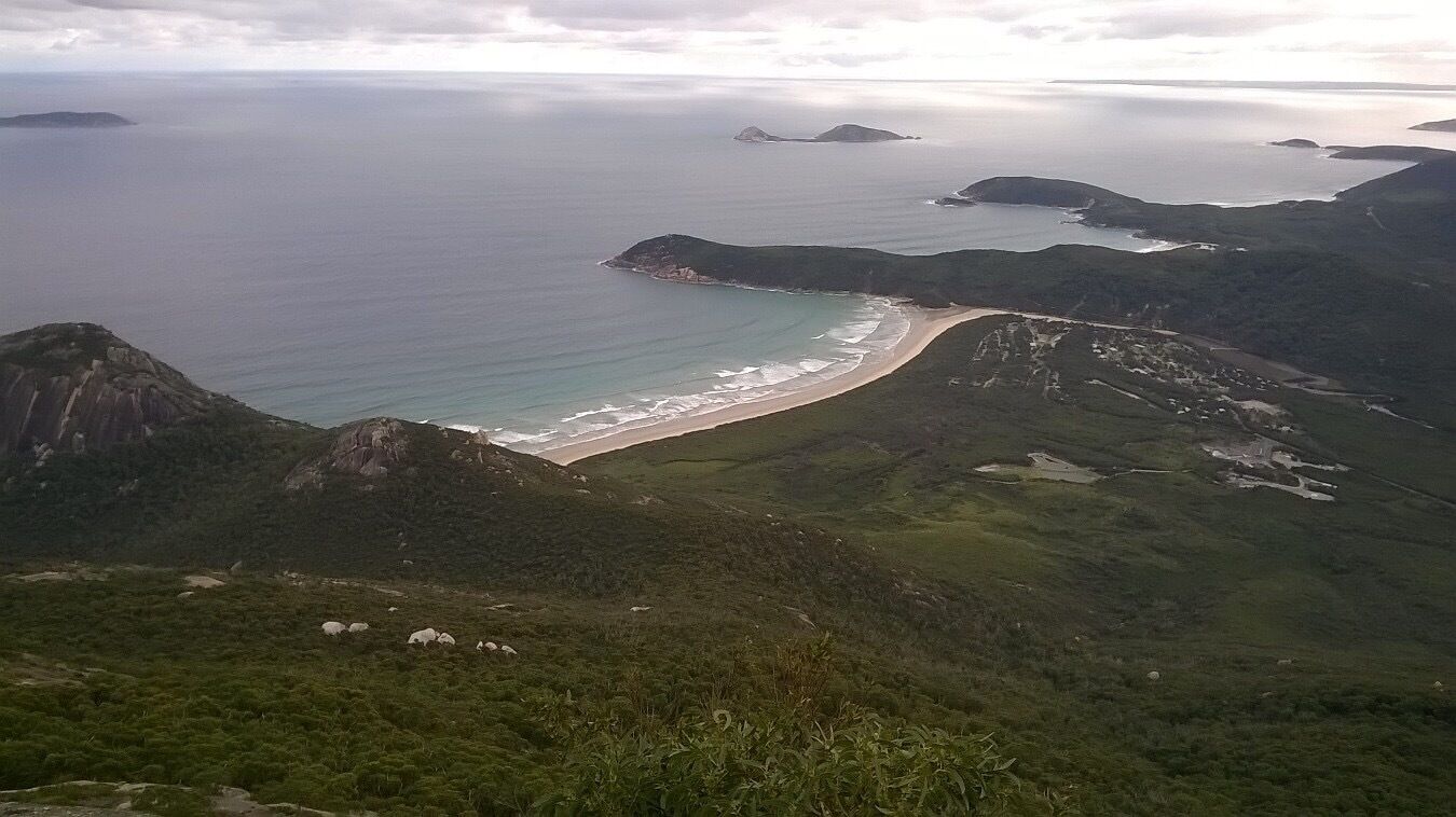 Un paisaje costero con playa, colinas rocosas y una isla distante.