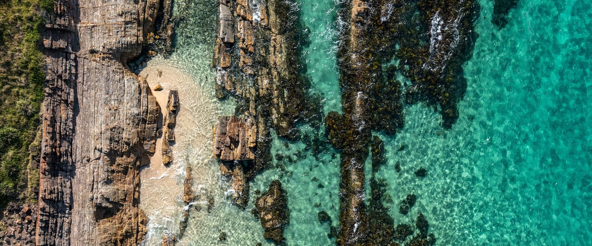 A rocky coastline with clear turquoise waters and a sandy beach.