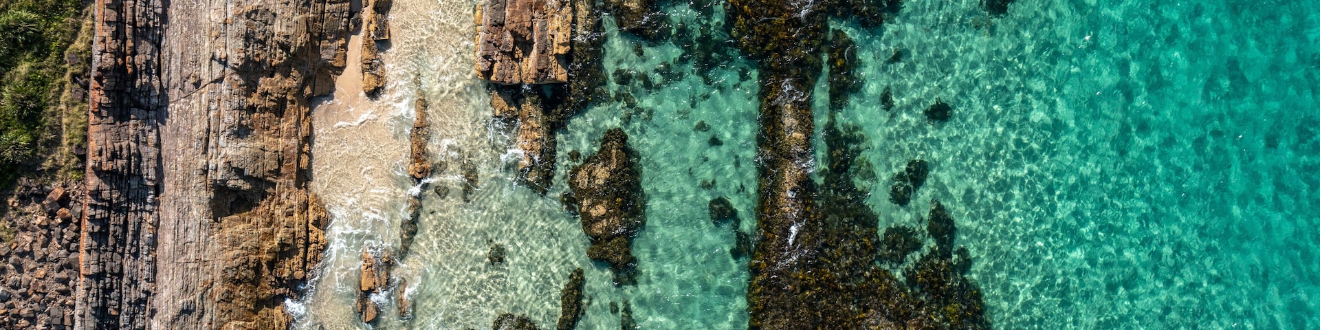 Litoral rochoso com águas turquesa cristalinas e uma praia arenosa.