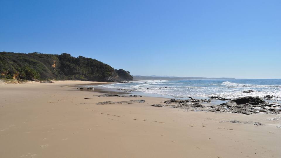 A sandy beach with rocky outcrops and a forested cliff.