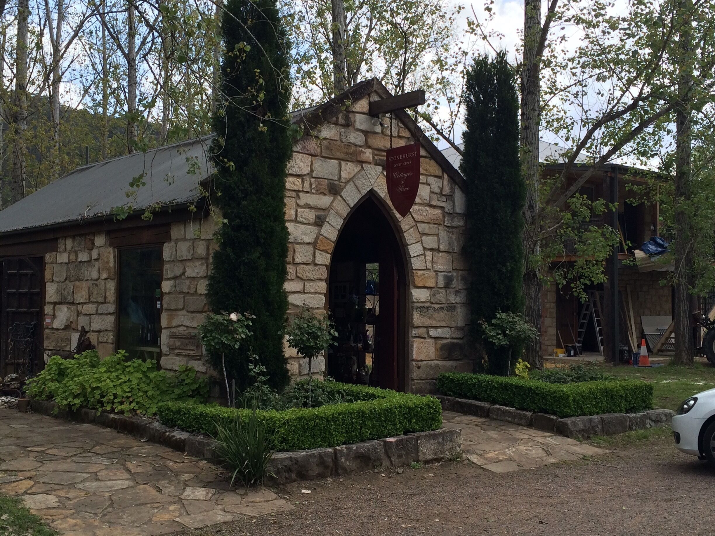 A stone building with a pointed arch doorway, surrounded by well-maintained hedges and a stone pathway.