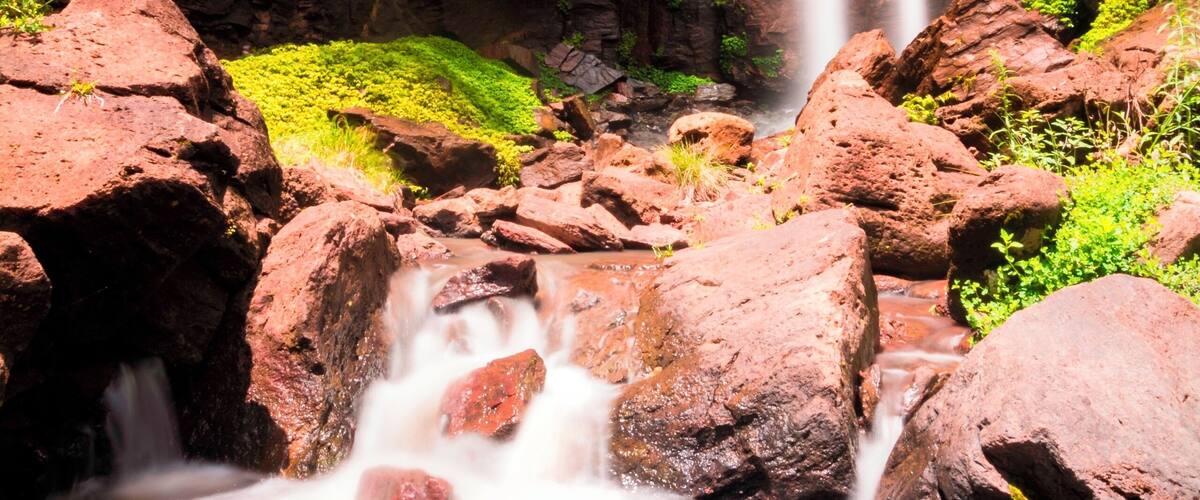 A waterfall cascading over red rocks with lush greenery around.