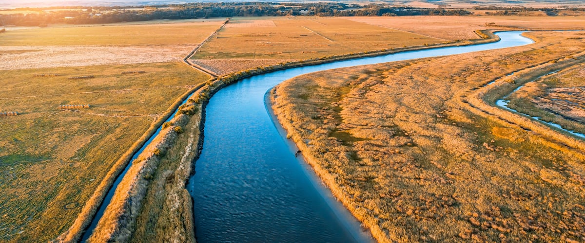 A river meandering through a flat landscape with fields on either side.