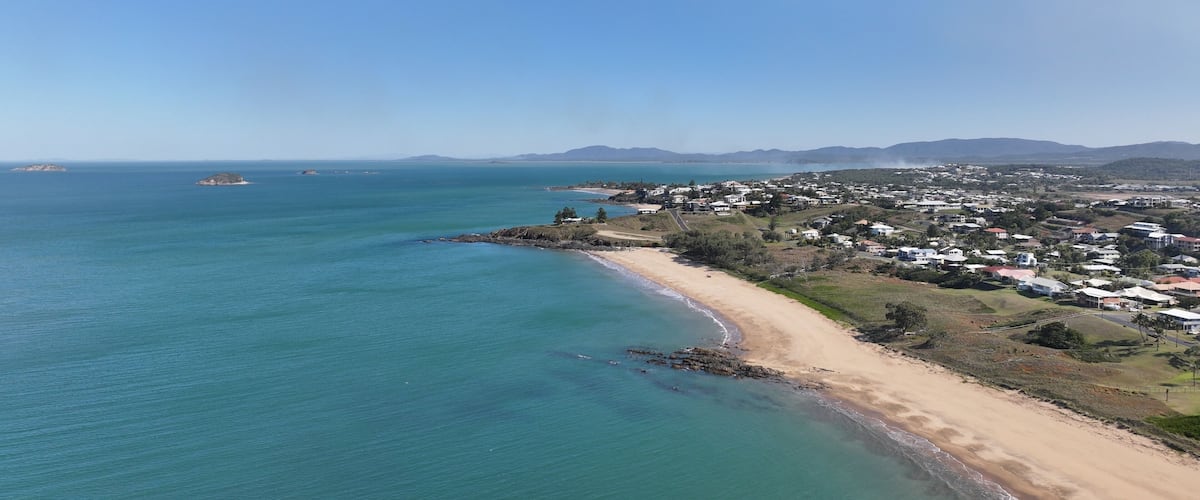 A coastal town with a beach, houses, and mountains in the distance.