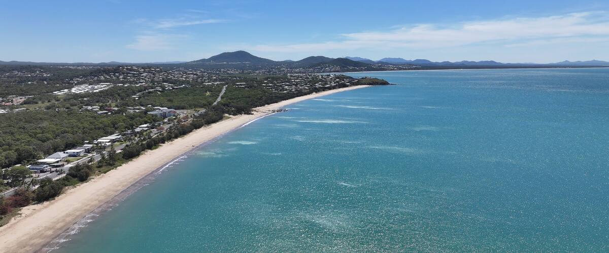 A coastal town with a beach, clear blue sea, and distant mountains.