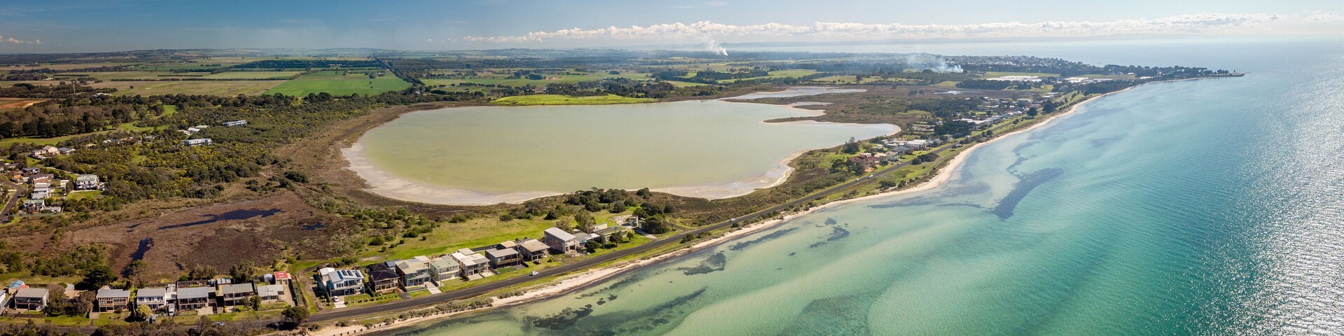 An aerial view of a coastal area with a large lake, a beach, and a residential area with houses and greenery.