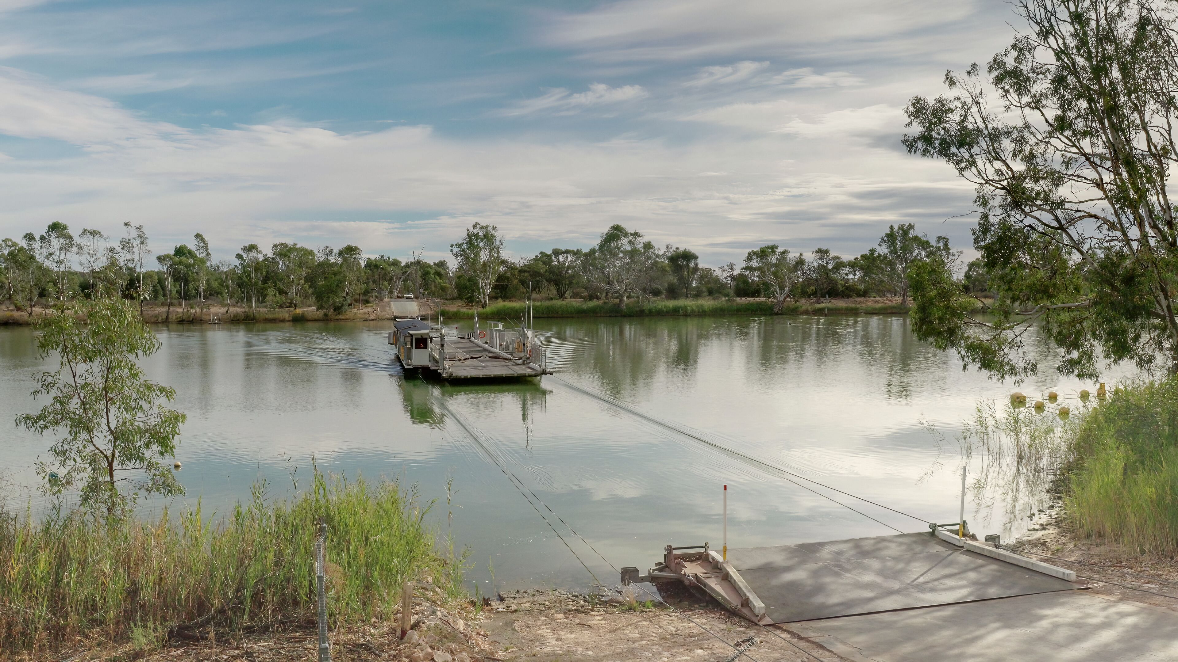 A calm lake with a small boat docked on the shore, surrounded by trees and vegetation.