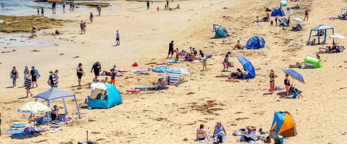 A crowded beach with people sunbathing, swimming, and walking along the shore.