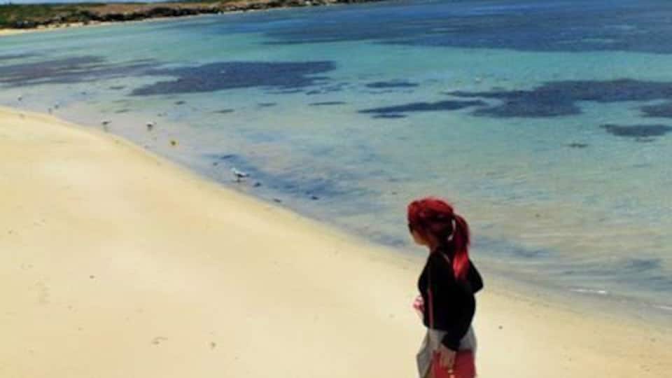 A sandy beach with clear turquoise water and a person walking.