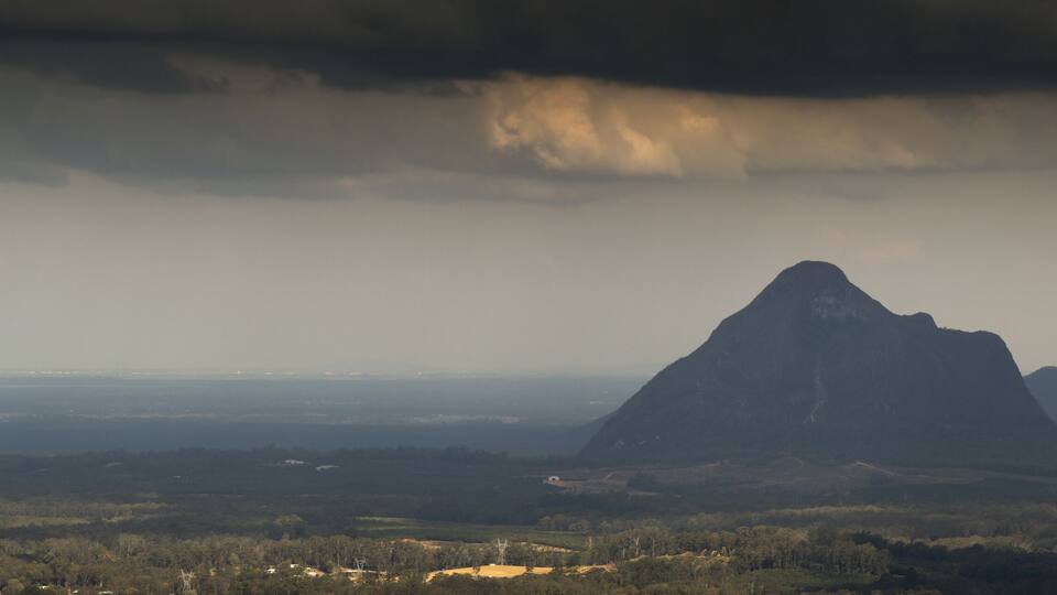 A mountain with a forested foreground and a cloudy sky.