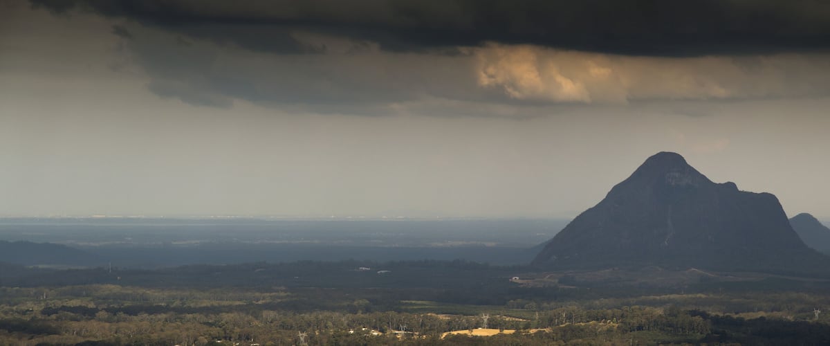 A mountain with a forested foreground and a cloudy sky.
