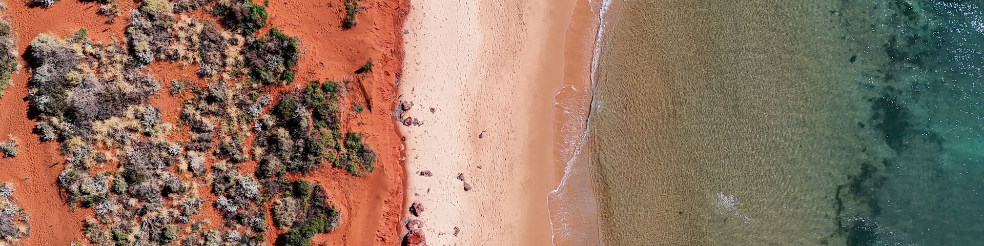 A beach with red sand and sparse vegetation.