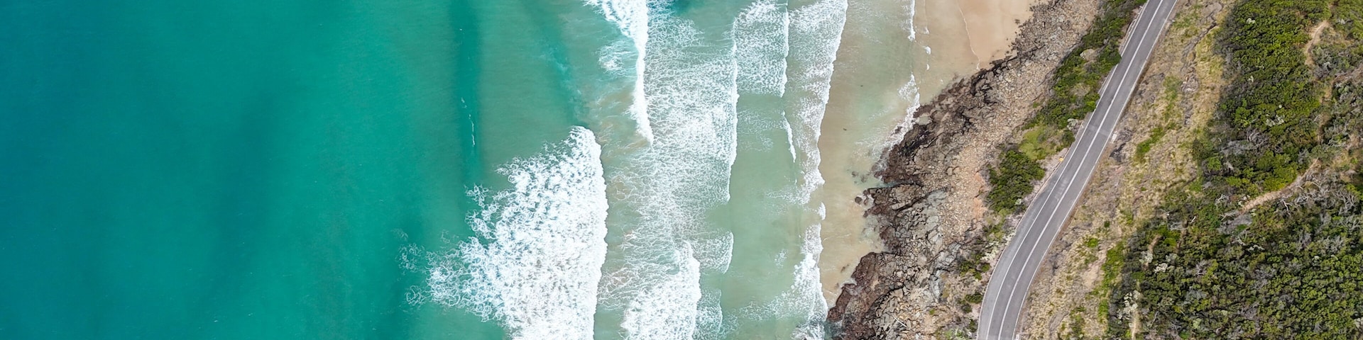 A coastal road with a beach and rocky cliffs.
