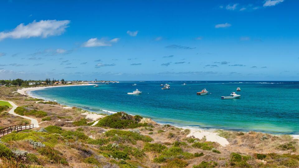 A coastal landscape with a clear blue sky, a sandy beach, and several boats anchored in the water.