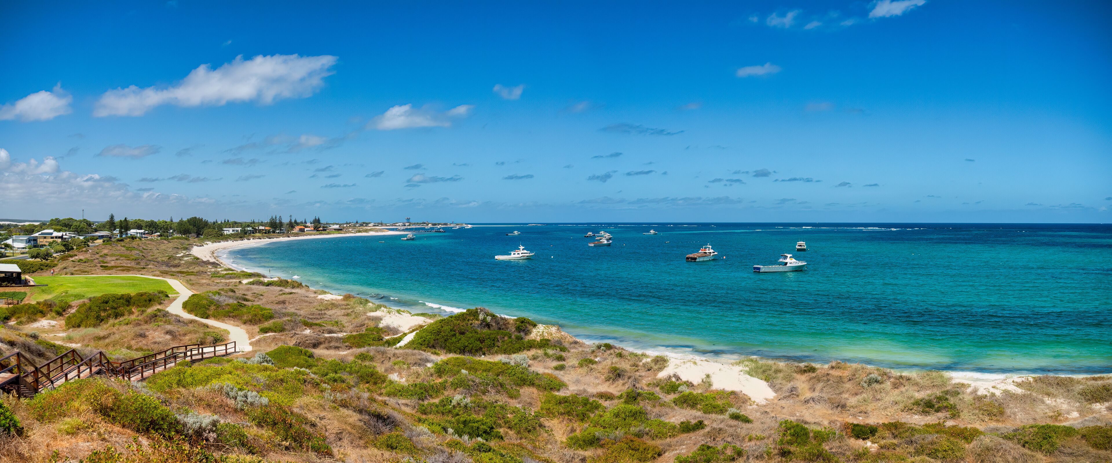 A coastal landscape with a clear blue sky, a sandy beach, and several boats anchored in the water.