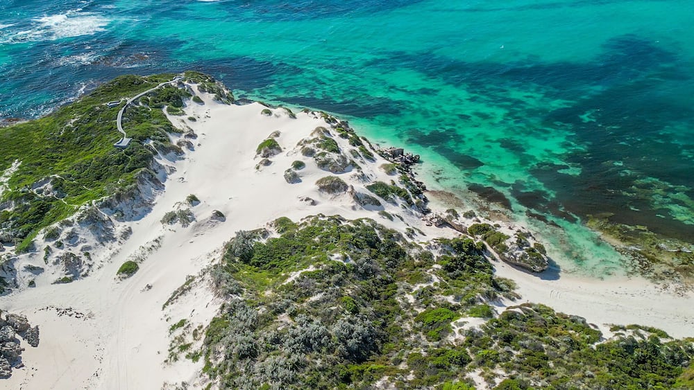 A coastal landscape with white sandy beaches, clear turquoise waters, and green vegetation.