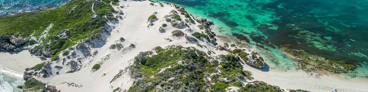 A coastal landscape with white sandy beaches, clear turquoise waters, and green vegetation.