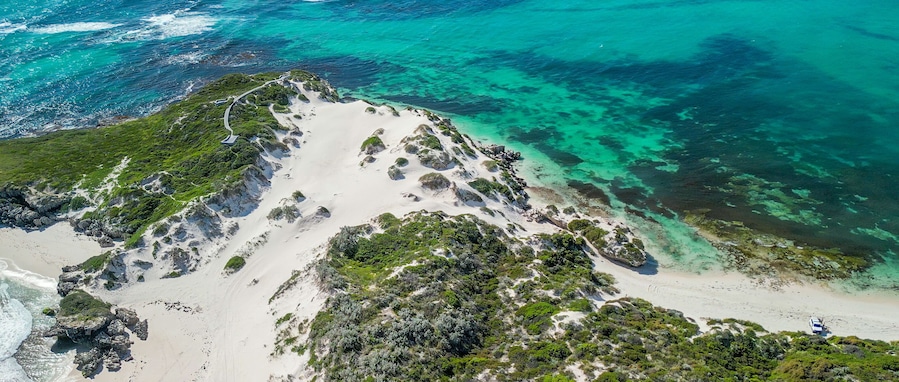 Paisagem costeira com praias de areia branca, águas turquesa cristalinas e vegetação exuberante.