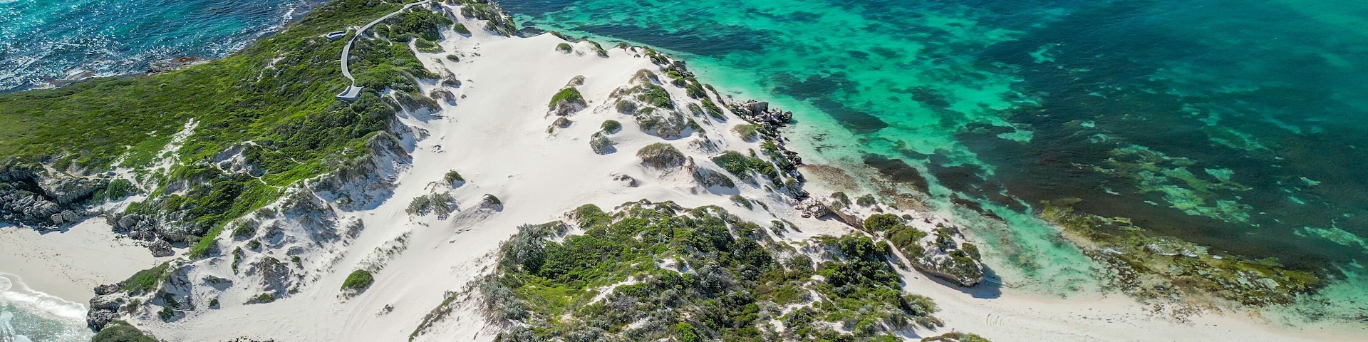 Un paisaje costero con playas de arena blanca, aguas turquesas cristalinas y vegetación verde.