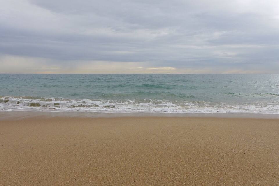 A beach with waves approaching the shore under a cloudy sky.