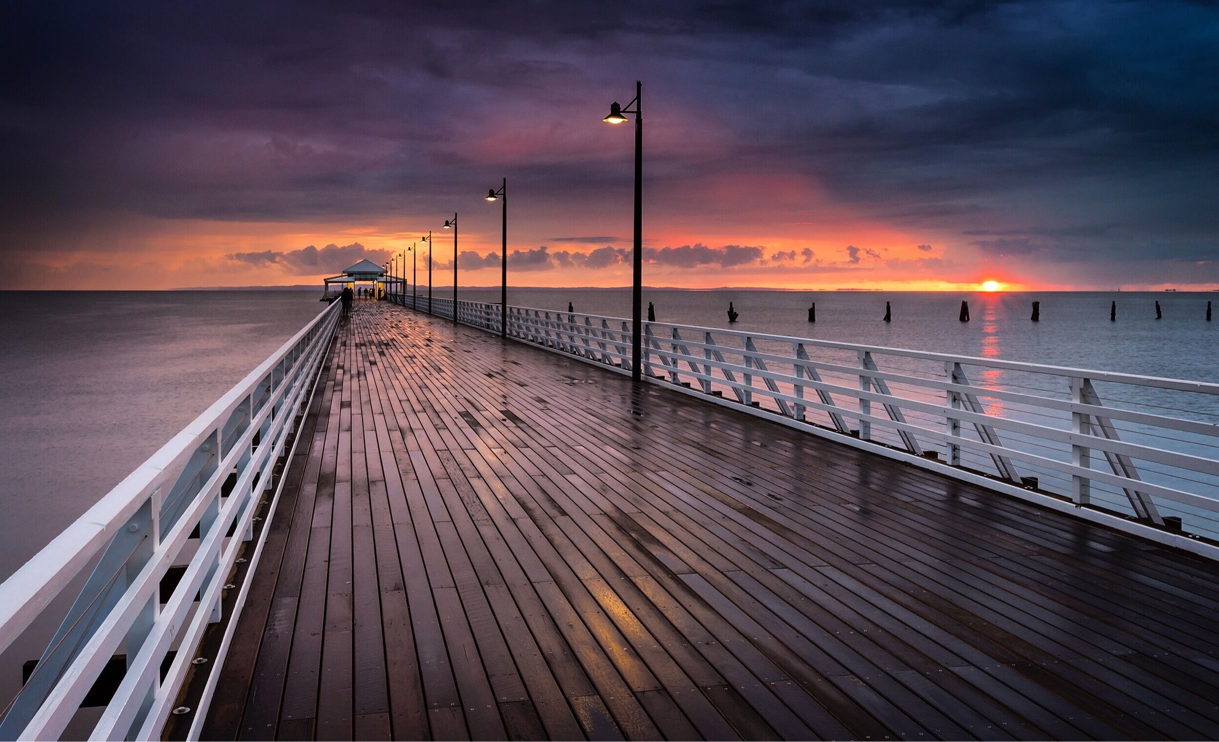 A wooden pier extending into calm waters at sunset with a cloudy sky.