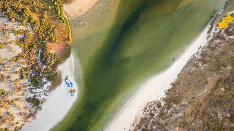 An aerial view of a beach with clear water, sandy shore, and some vegetation.