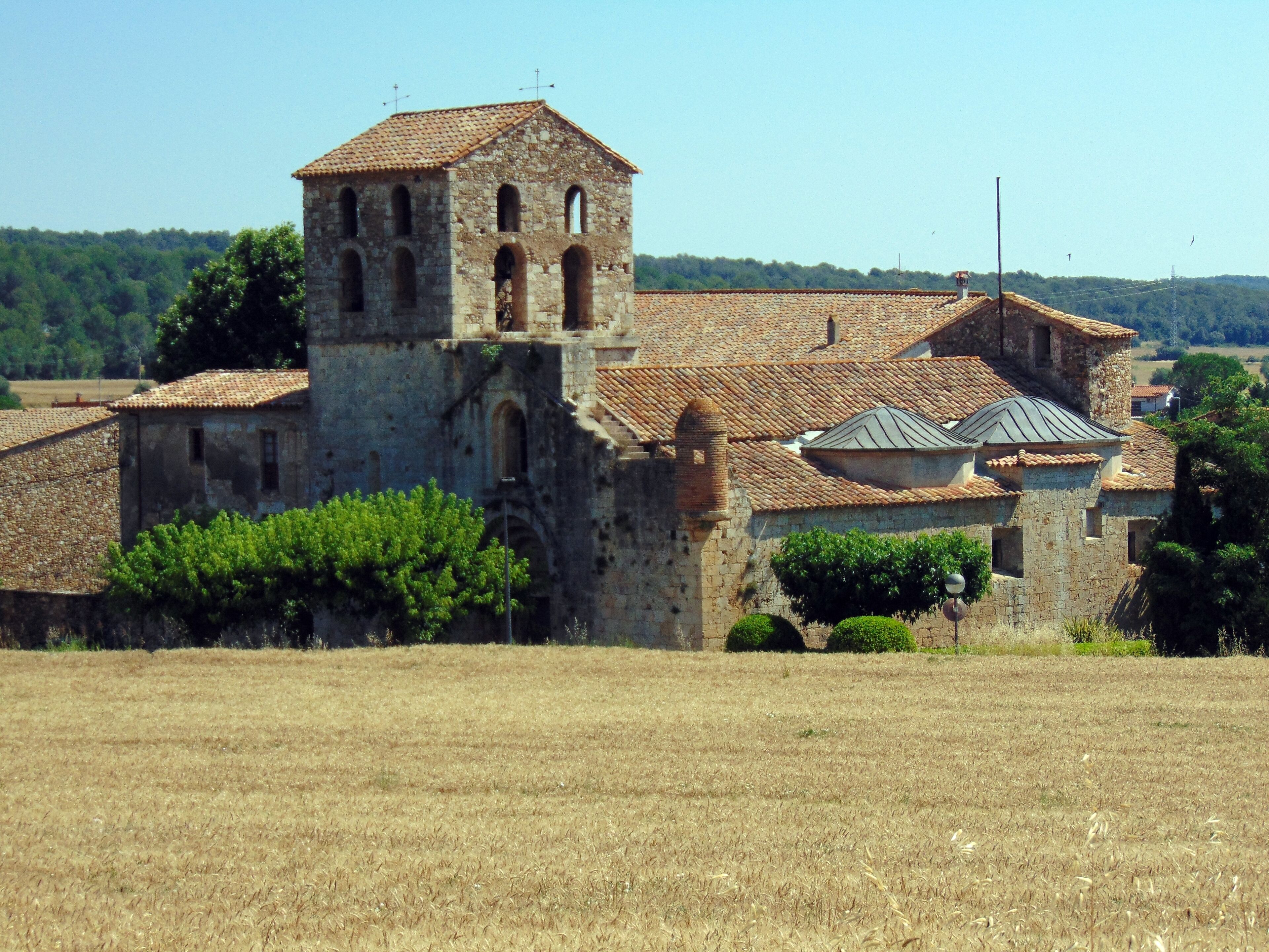A historic stone church with a bell tower, surrounded by fields and trees.