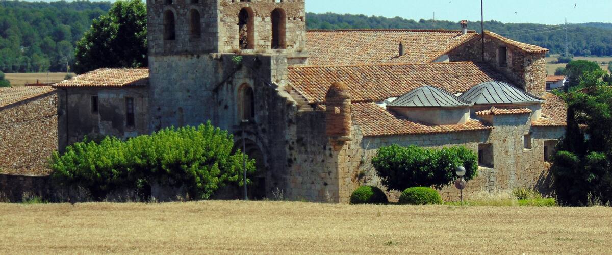A historic stone church with a bell tower, surrounded by fields and trees.