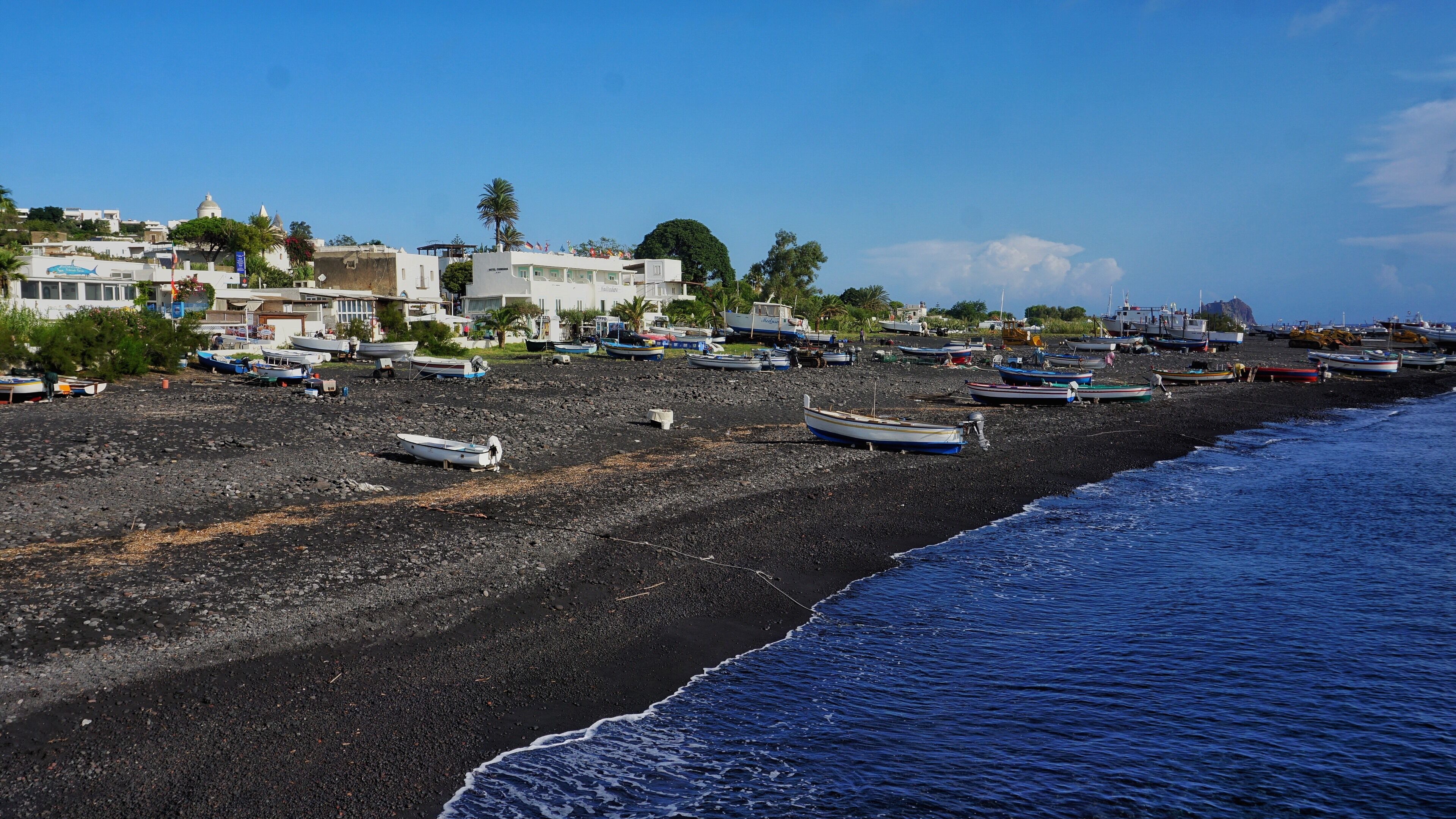 A beach with numerous boats and a rocky shoreline.