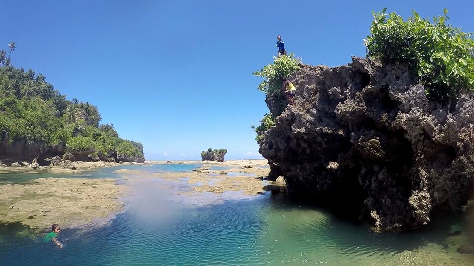 A coastal landscape with clear turquoise waters, rocky formations, and lush greenery.