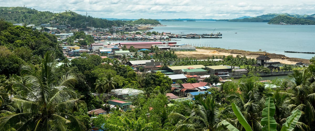 A coastal town with a harbor, buildings, and lush greenery.