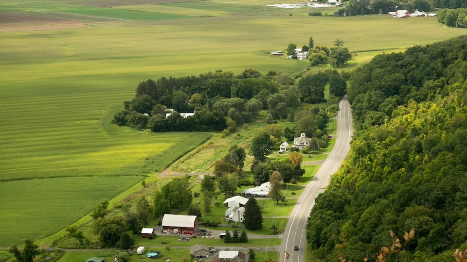 A winding road through a rural landscape with green fields, scattered houses, and a hill in the background.