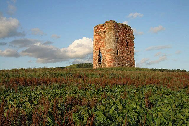 A historic stone tower in a grassy field with a clear sky.