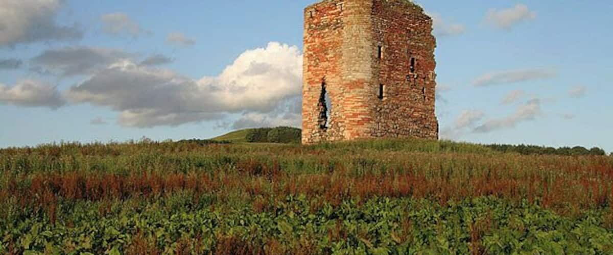 Ein historischer SteinTurm in einem grasbewachsen Feld unter blauem Himmel.