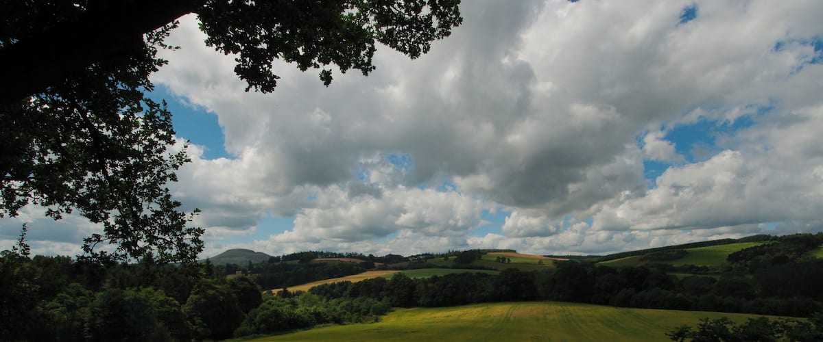 A rolling green landscape with hills and a cloudy sky.