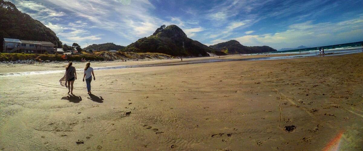 A beach with footprints, a rainbow, and mountains in the background.