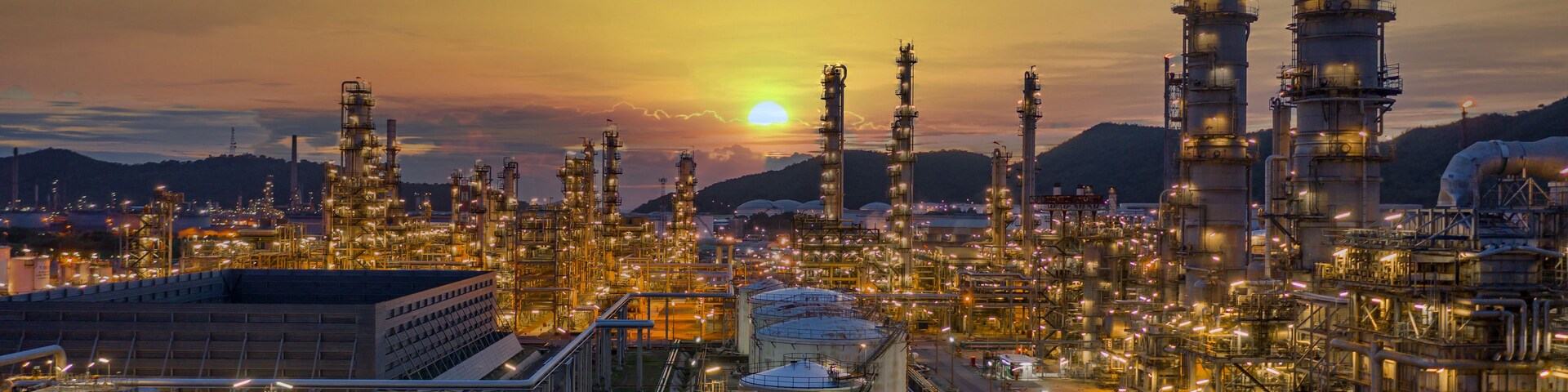 Un complejo industrial con varias estructuras altas y tanques de almacenamiento, frente a un cielo al atardecer.