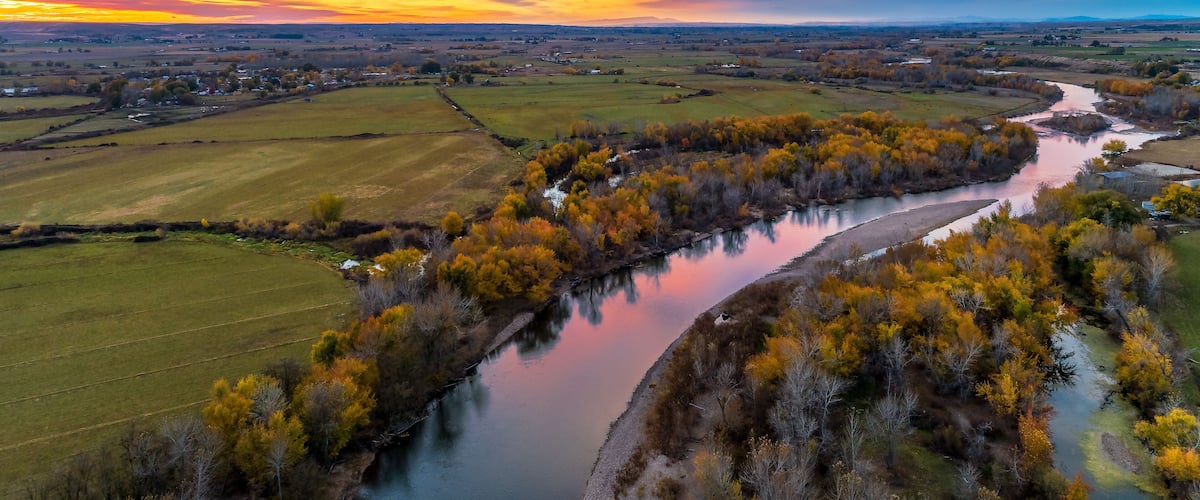 A river winding through a valley with autumn foliage and a sunset sky.