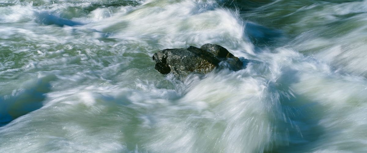 A turbulent river with a large rock in the center.