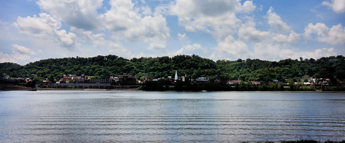 A lake with a town on a hill, surrounded by greenery and a partly cloudy sky.