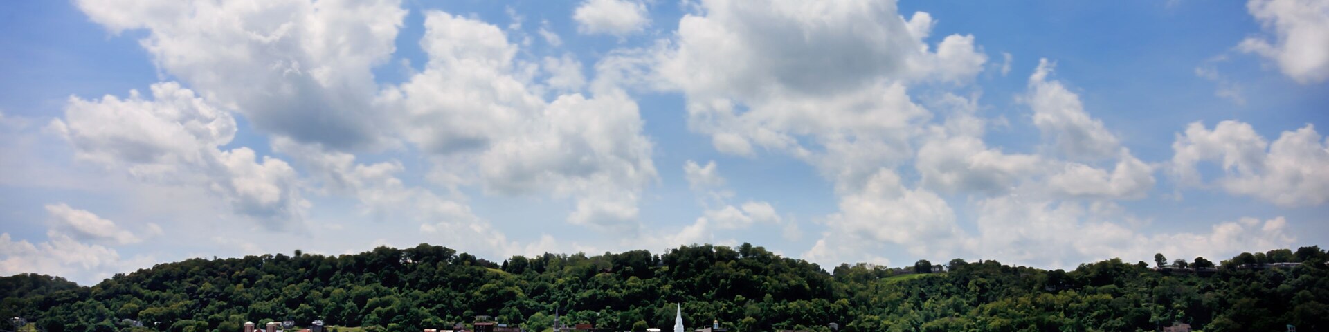 A lake with a town on a hill, surrounded by greenery and a partly cloudy sky.