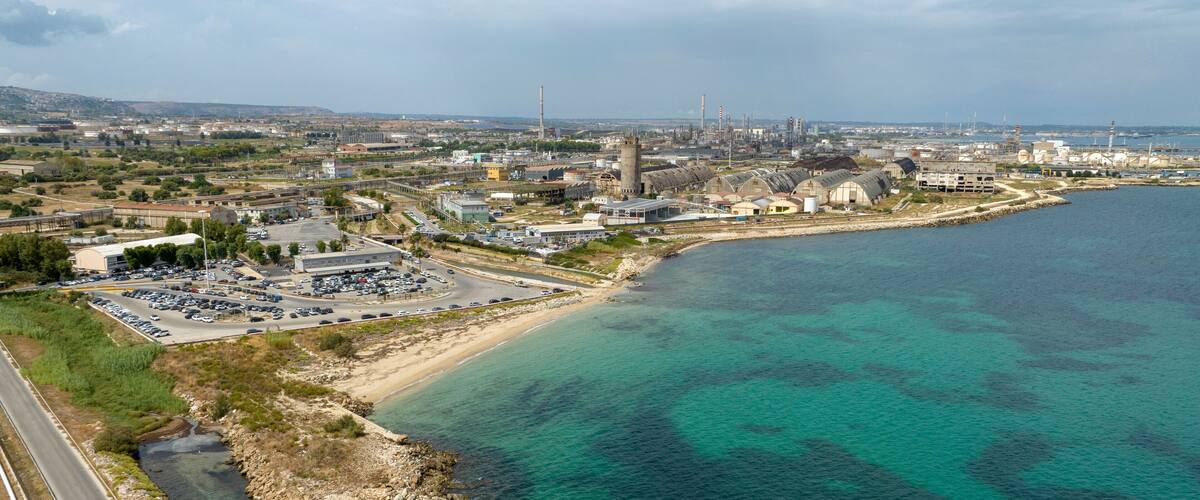 An industrial area with a large parking lot, a beach, and a body of water.