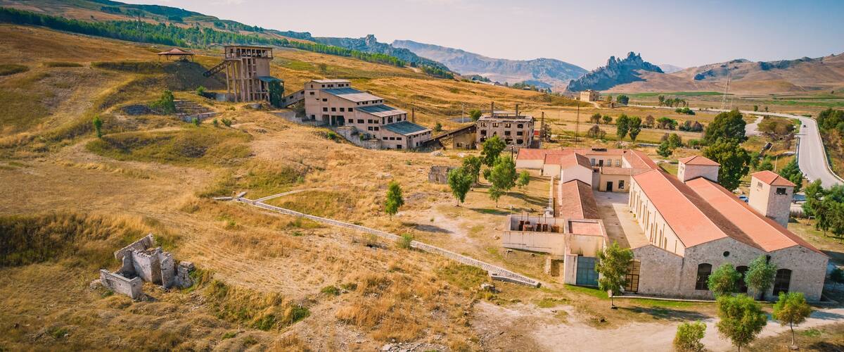 An abandoned industrial complex with buildings and structures amidst a hilly landscape.