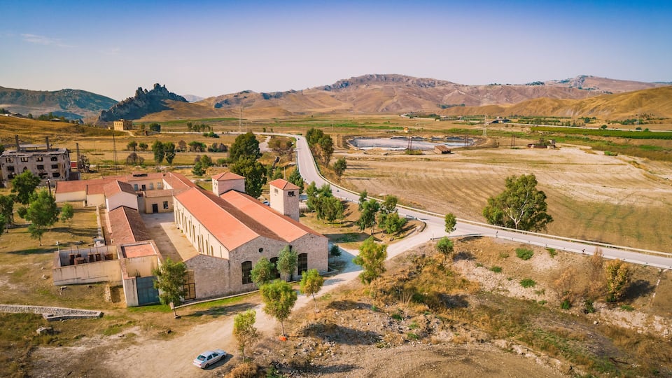 A rural landscape with a church, a road, and surrounding hills.